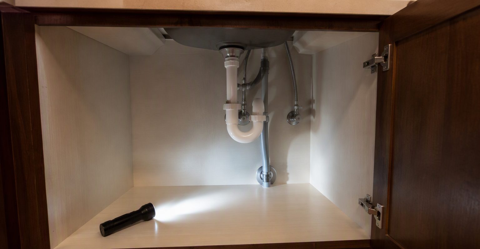 Flashlight beam inspecting a clean empty cabinet under a rental kitchen sink